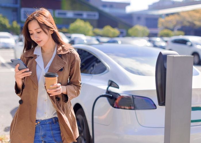 Woman charging EV looking at cell phone-1